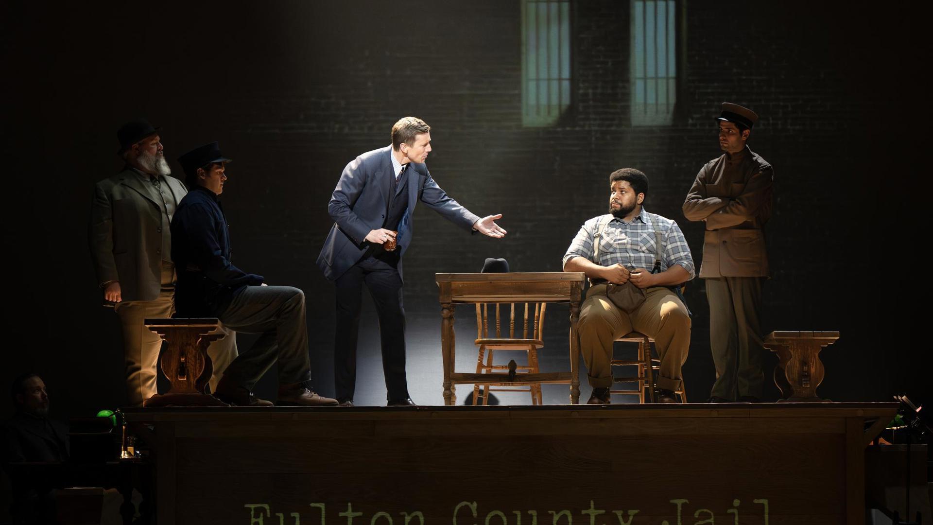 A man speaking to another man in a chair. Three other people surround them.