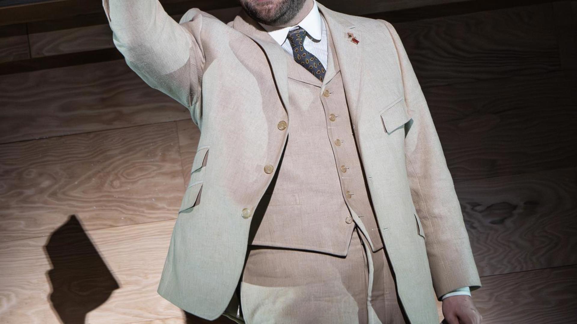 A man in 1910s attire holding a book in the air.