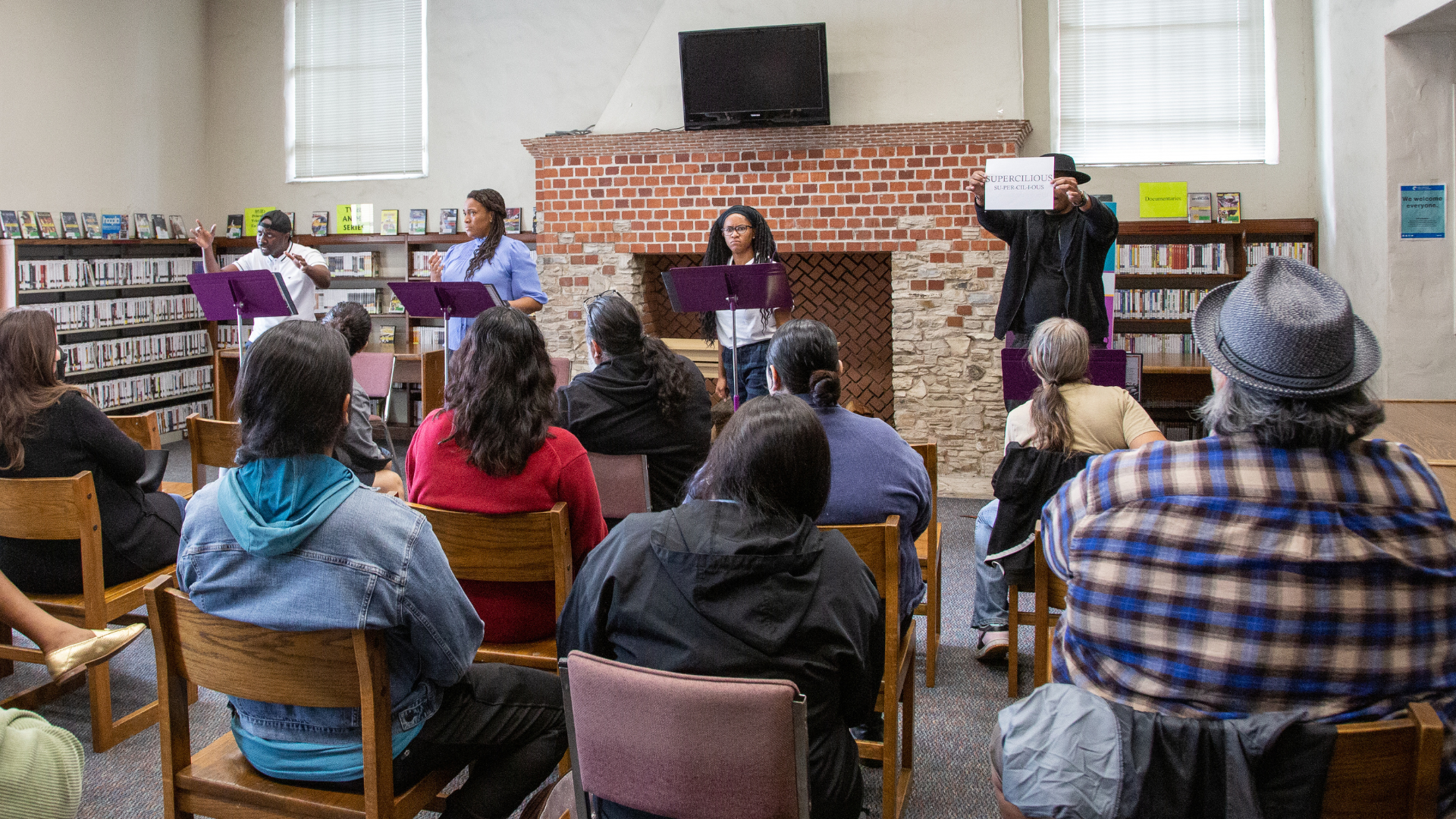 An small audience enjoys a play reading in a public library. 