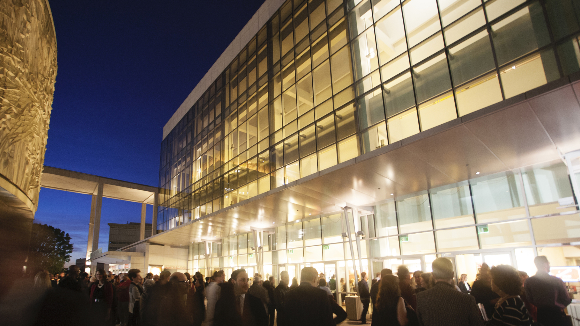 A photo of a brightly lit building at night with many people walking around the outside in a blur