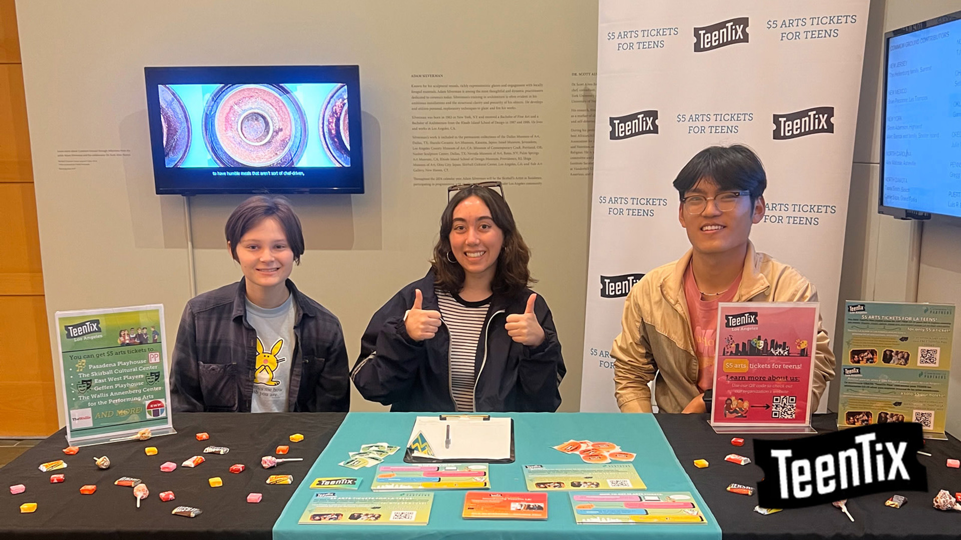 Three teens sit behind a table with TeenTix flyers and candy. 