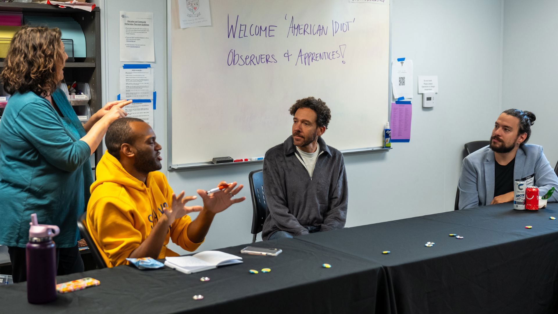 Three people sit in front of a thin black table having a conversation while an ASL interpreter interprets the conversation.   