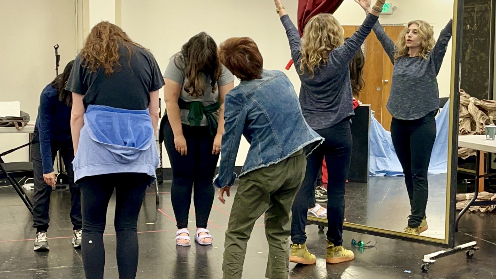 A group of people stretch and roll their necks in a rehearsal room. 