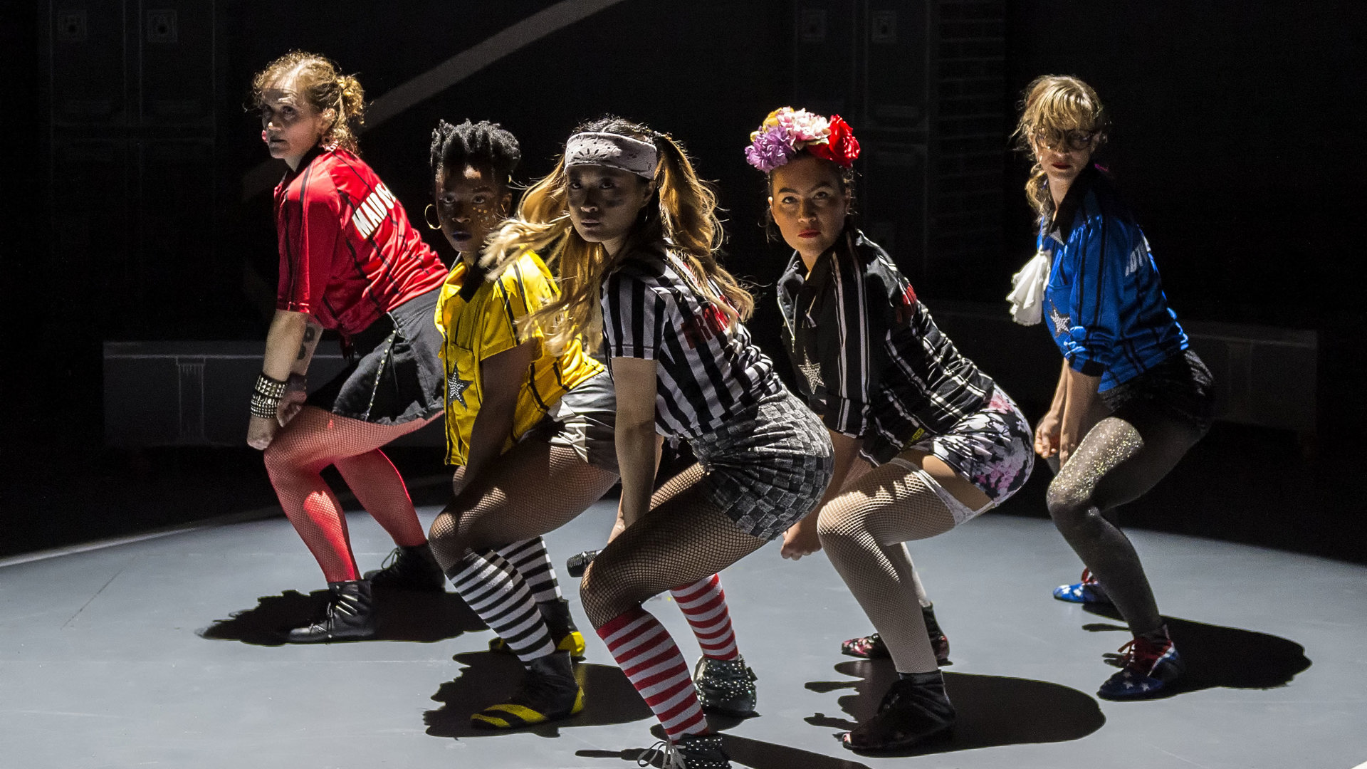 Five actors squat onstage during a performance.