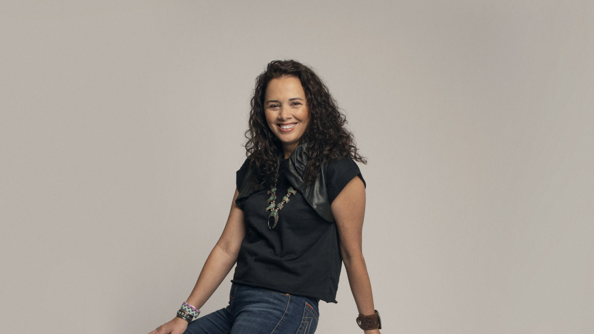 Larissa FastHorse poses on a white stool. 