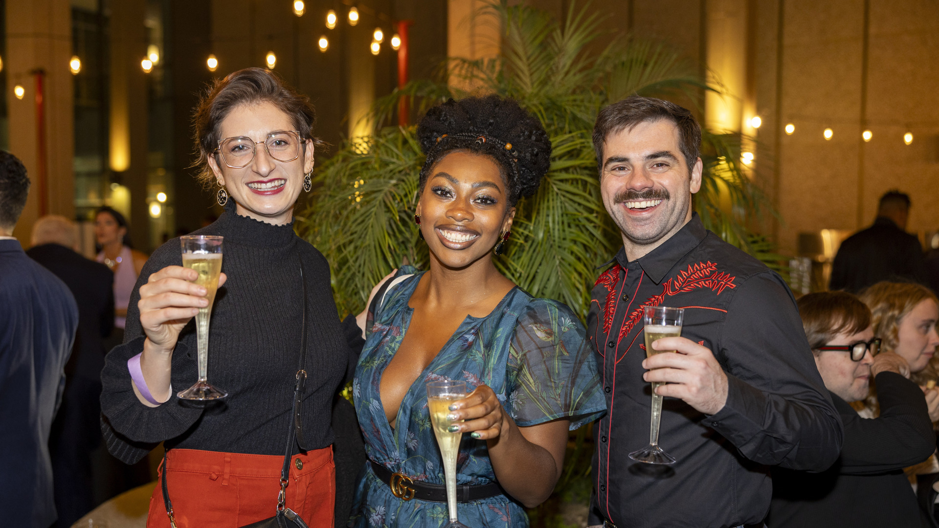 Three patrons smile while holding champagne. 