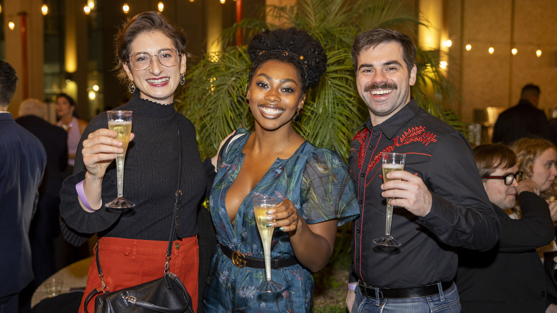 Three patrons smile while holding champagne. 