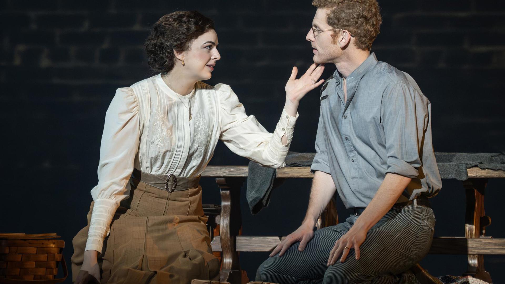 A woman caresses a man's face while they kneel on the floor.