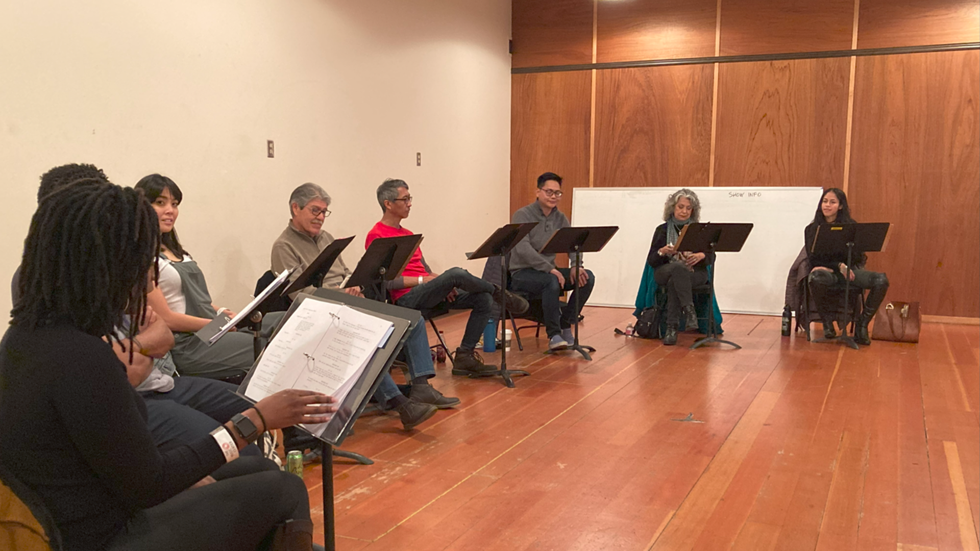 A row of playwrights read through scripts placed on music stands. 