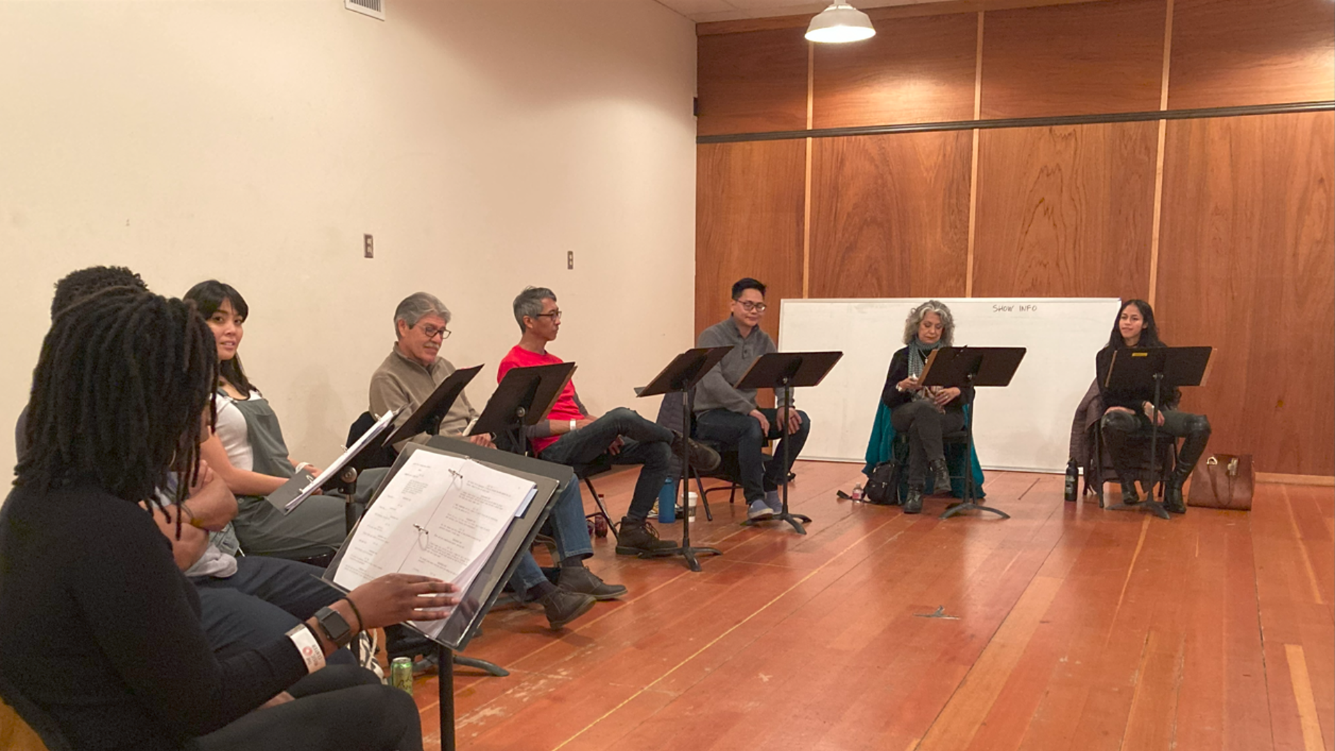 A row of playwrights read through scripts placed on music stands. 