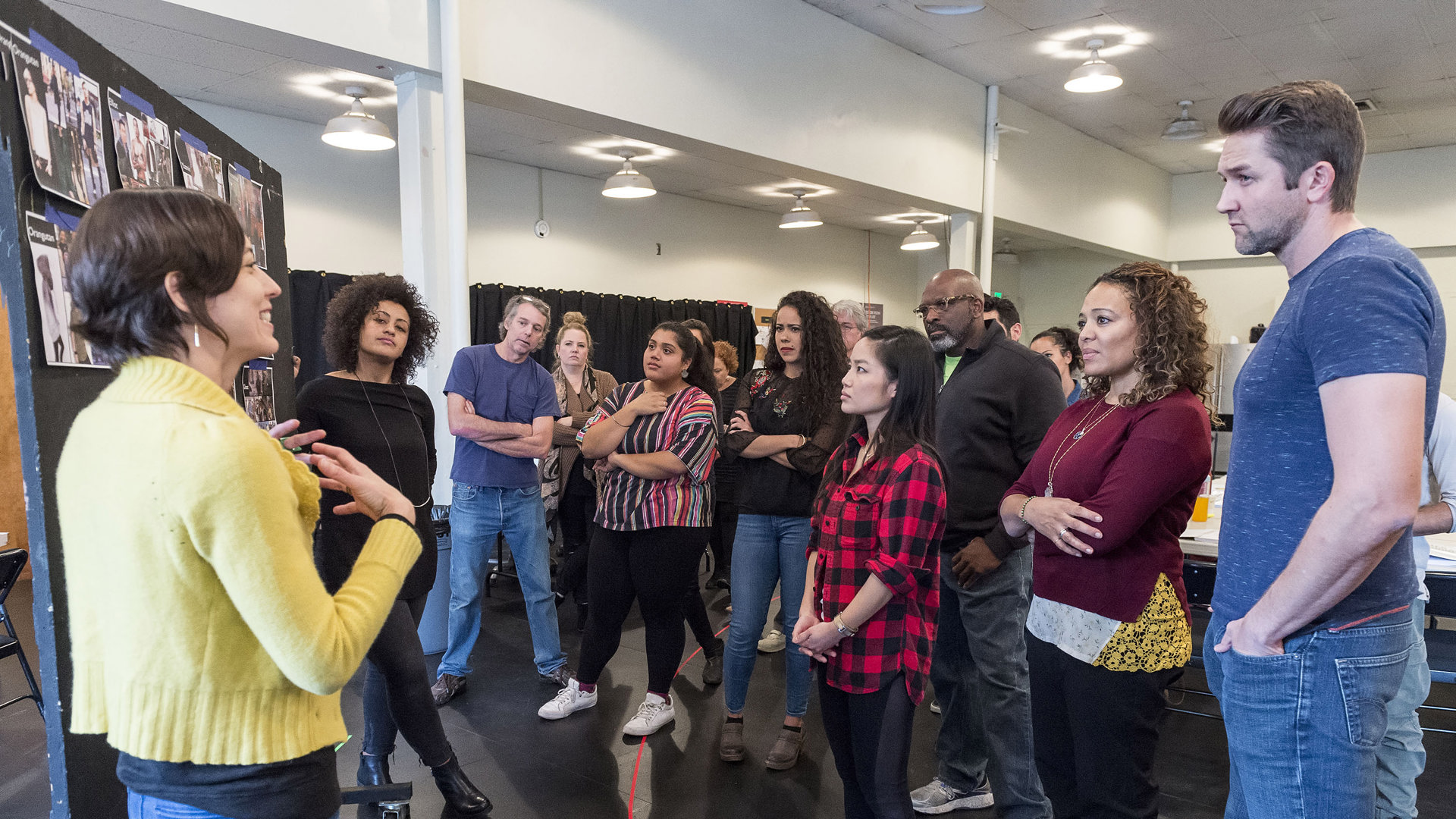 A group of theatre artist stand in front of a board review pinned images. 