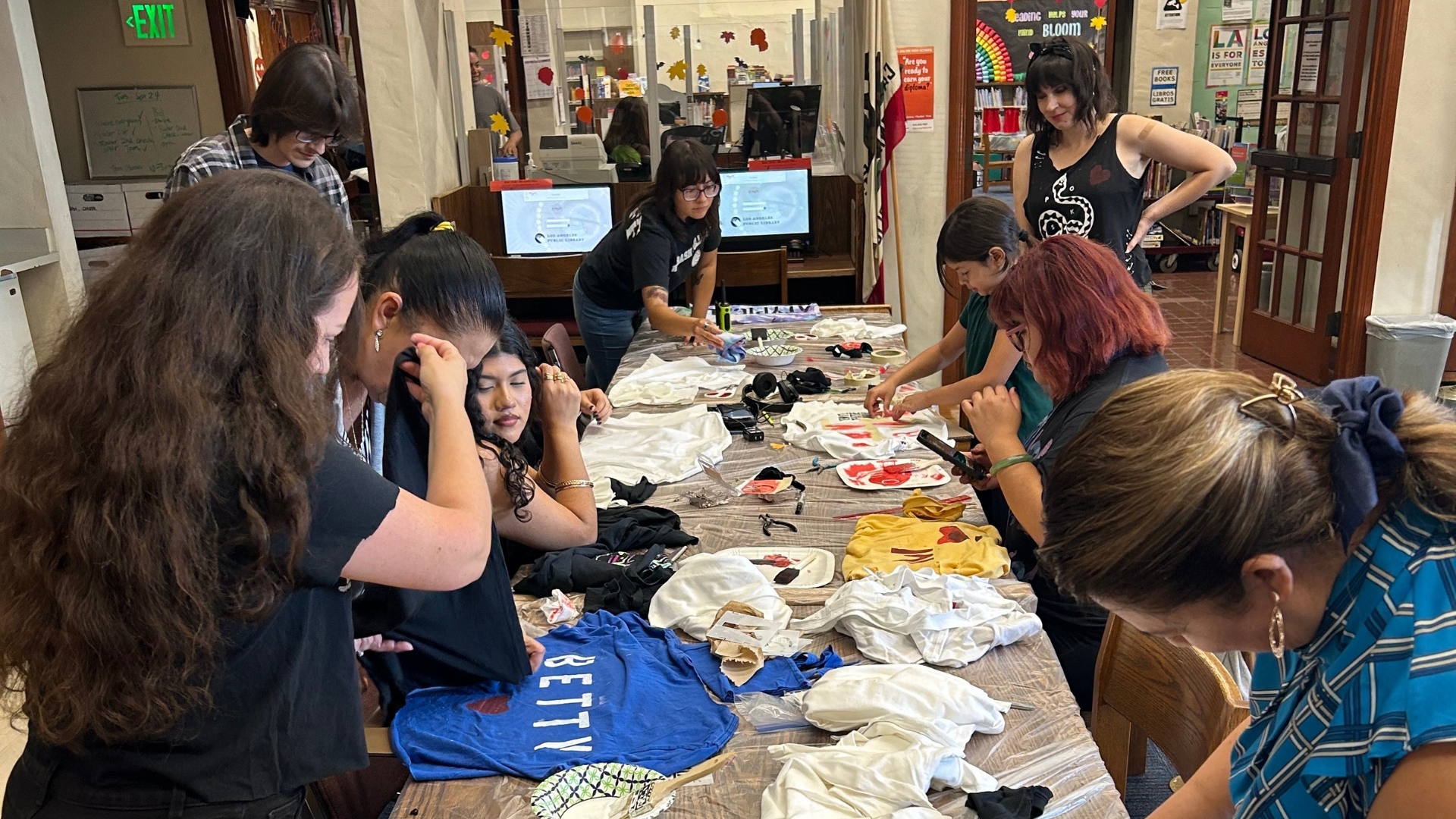 A table full of children and parents do crafts with shirts. 