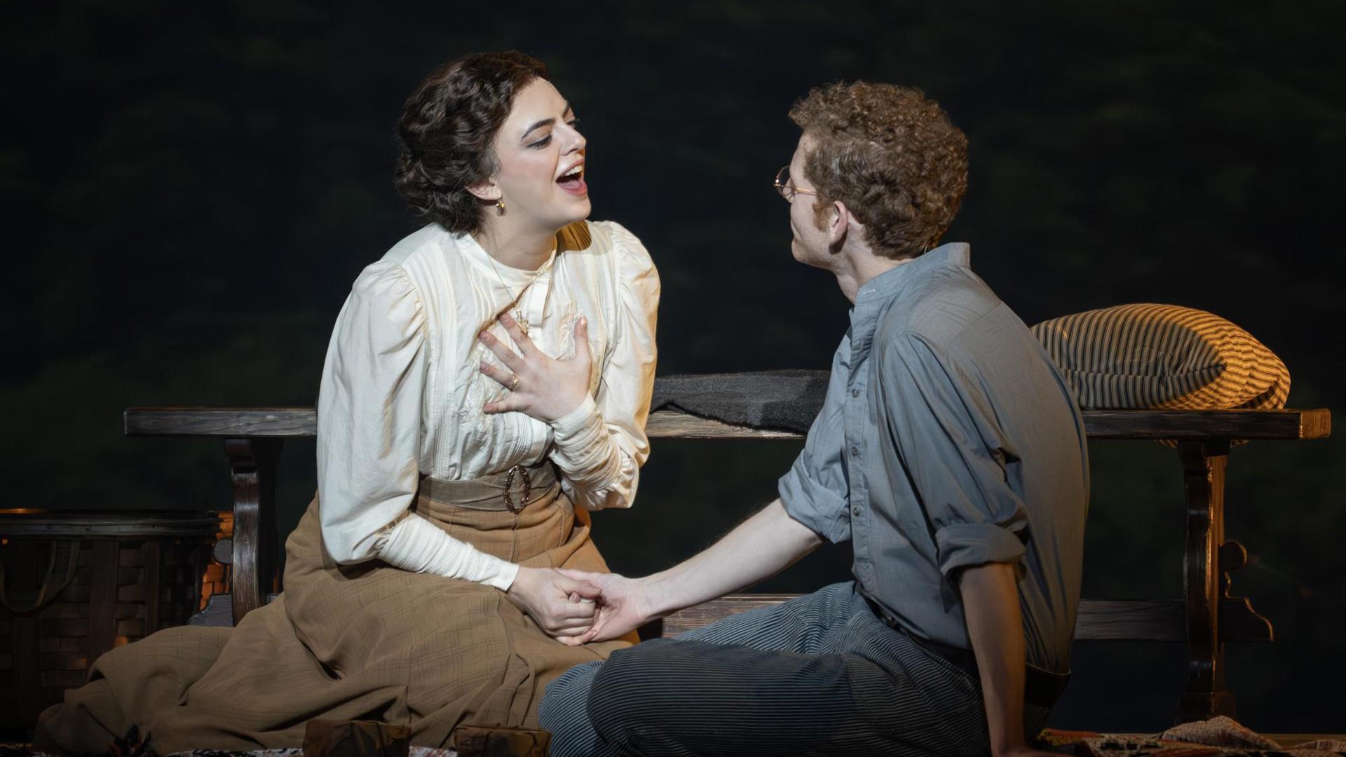 A man and woman sitting on the floor, holding hands and singing